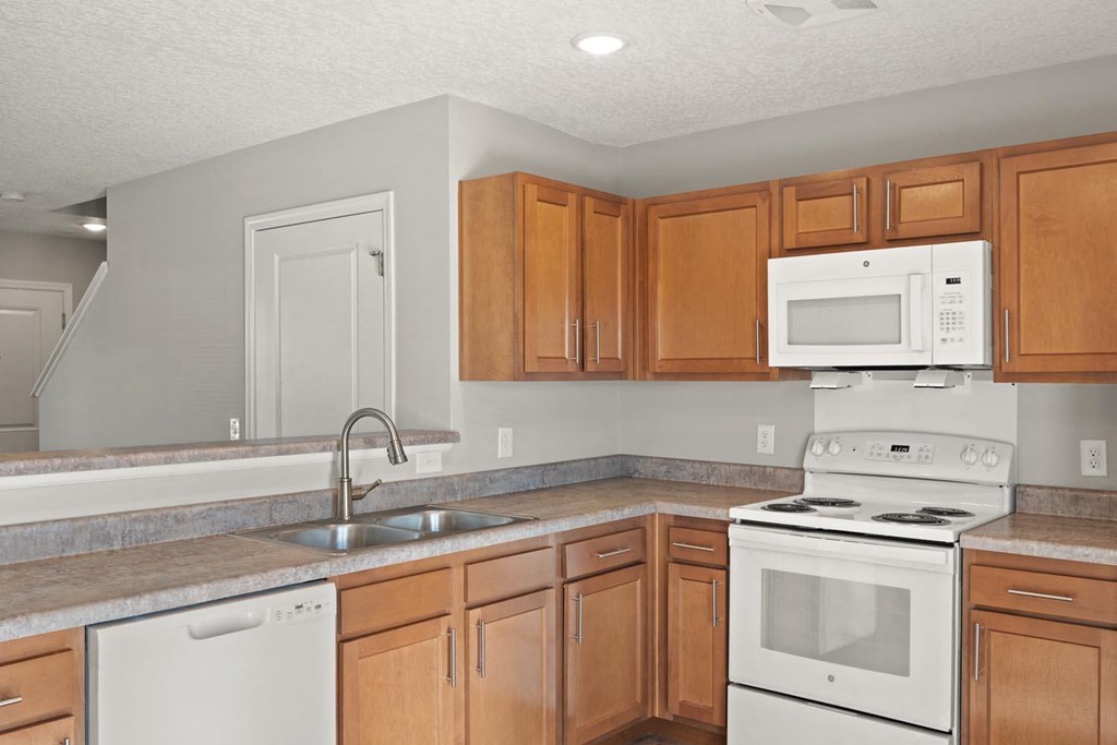 A kitchen with a white dishwasher, white stove, and brown cabinets.