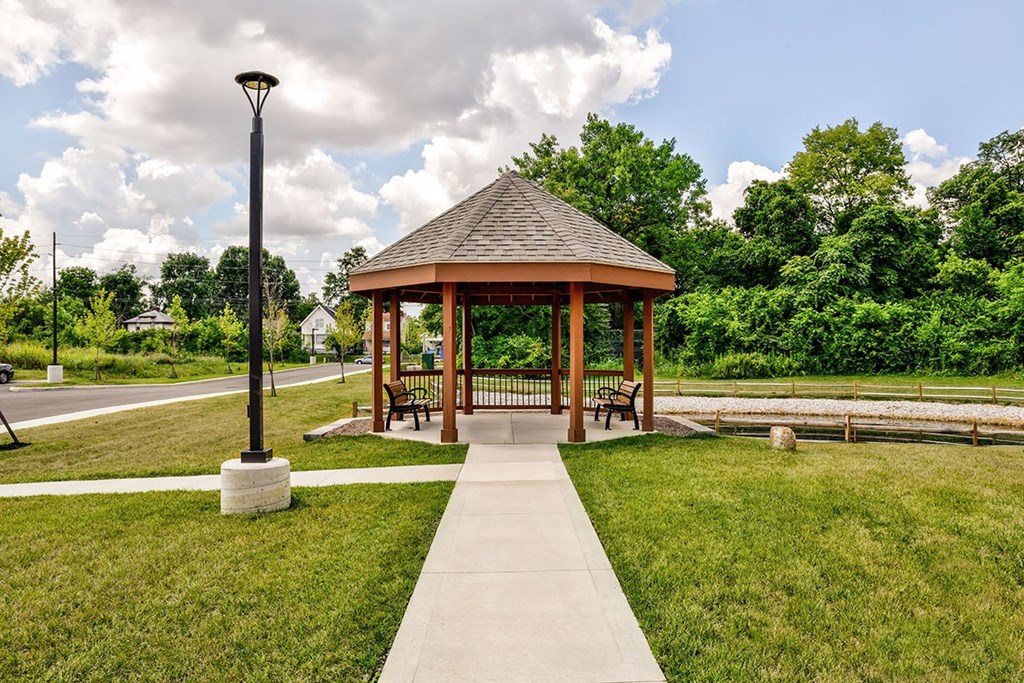 A gazebo is surrounded by a grassy area and a concrete walkway.