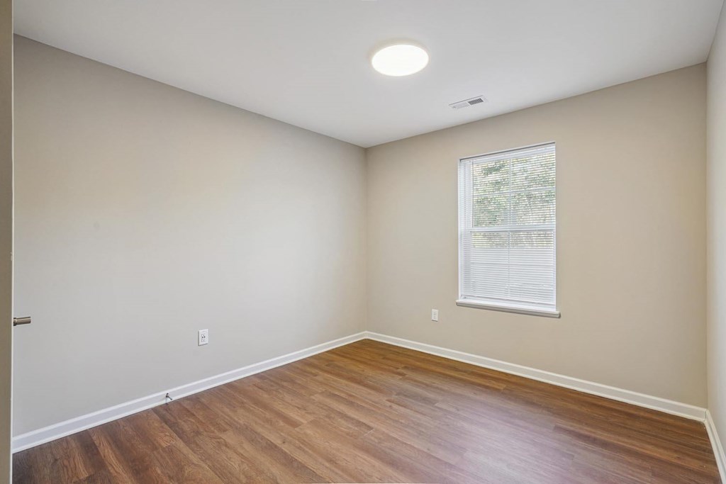 A room with wooden flooring and a window with blinds.