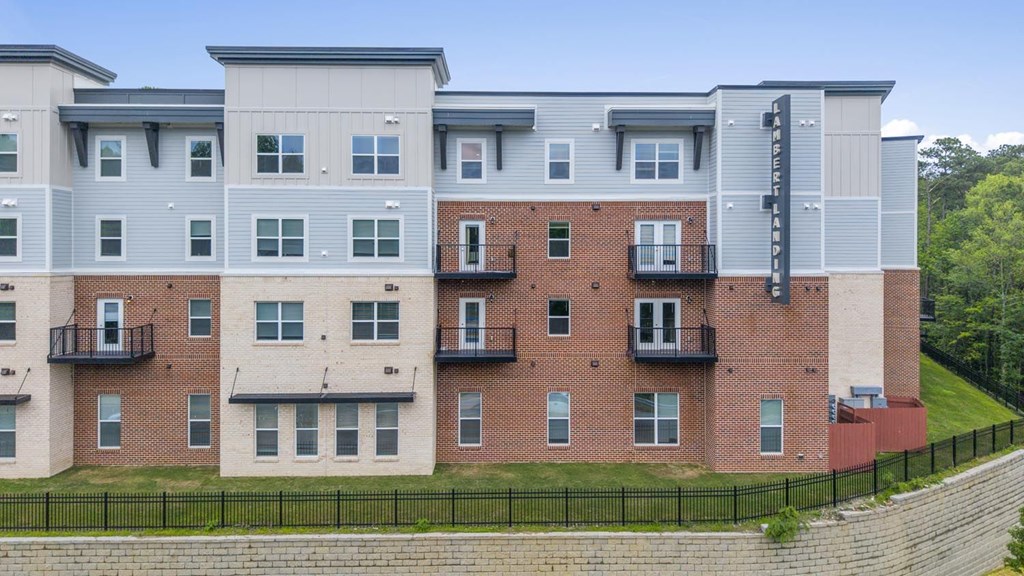 A multi-story apartment building with balconies and a black fence in front.
