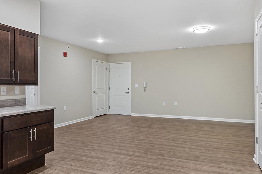 an empty living room with wood flooring and a kitchen