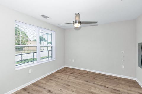 A room with a ceiling fan and a window overlooking a fence.