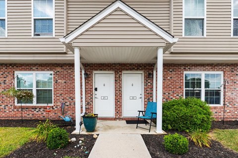 the front porch of a brick house with two white doors and a blue chair