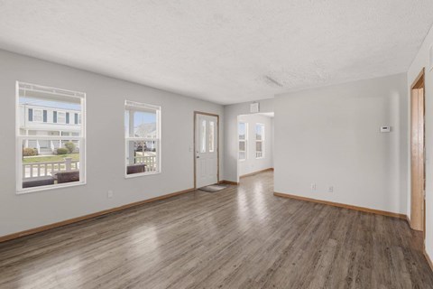 A spacious room with wooden floors and white walls, featuring two windows with pictures on them.