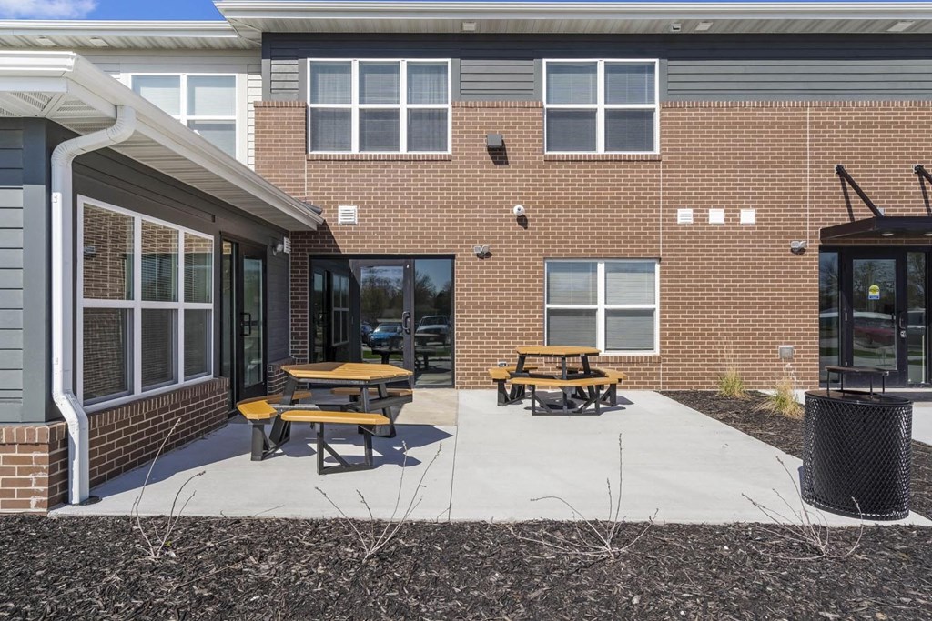 a patio with two picnic tables in front of a brick building