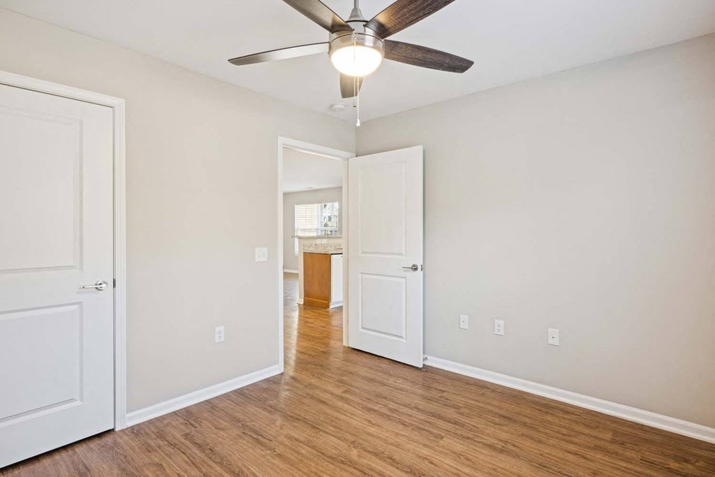 an empty living room with a ceiling fan and a door to a bathroom
