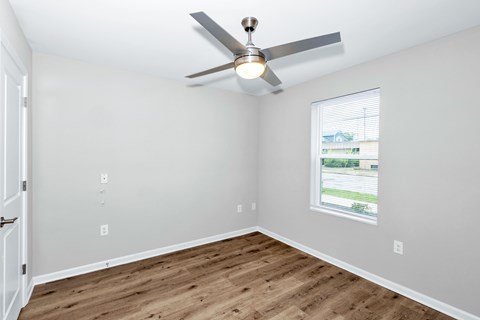 A room with a ceiling fan and a window showing a view of a green area outside.
