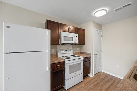 A white refrigerator is in a kitchen with a white microwave and white stove.