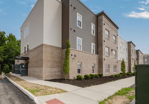 A modern apartment building with a brick facade and a landscaped front yard.