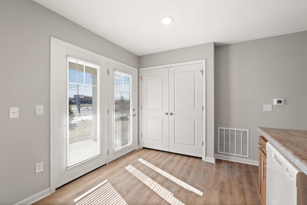 A room with a white door, a window with blinds, and a wooden floor with a rug.