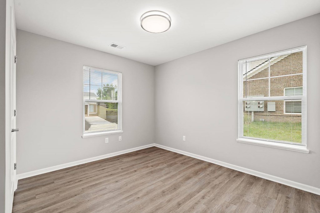 A room with a window showing a view of a house and a wooden floor.