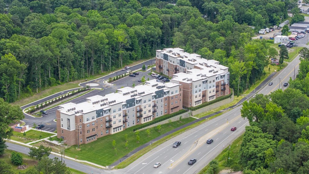 A large apartment complex is surrounded by trees and a busy road.