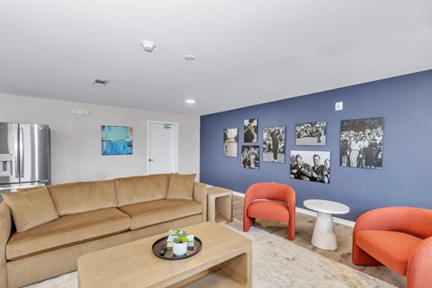 A living room with a brown sofa, orange chairs, and pictures on the wall.