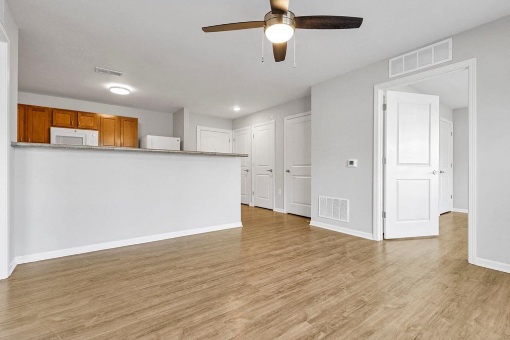 an empty living room with a kitchen and a ceiling fan