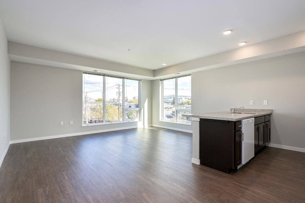 an empty living room with a kitchen and a large window