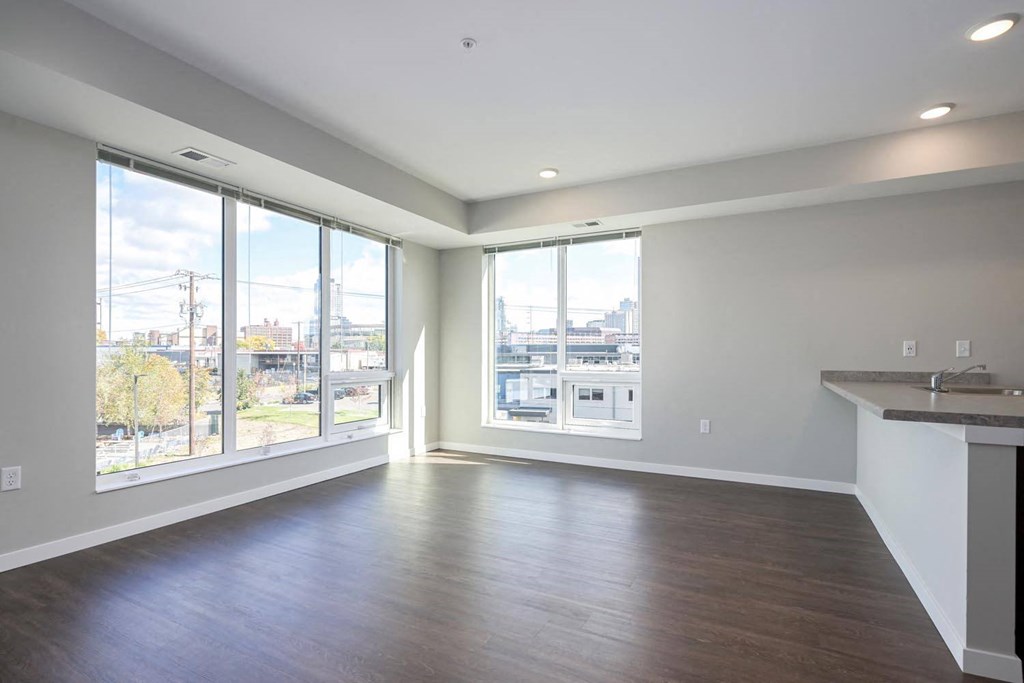 the living room of an apartment with a large window and wooden floors