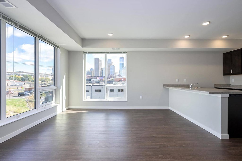 an empty living room with a large window and a kitchen