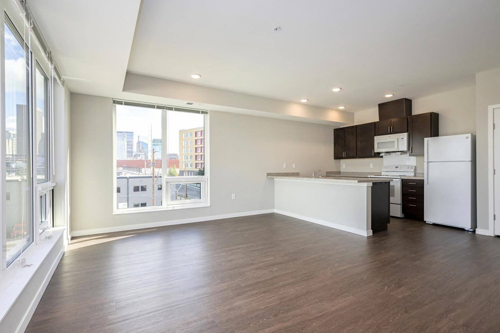 an empty living room with a kitchen and a large window