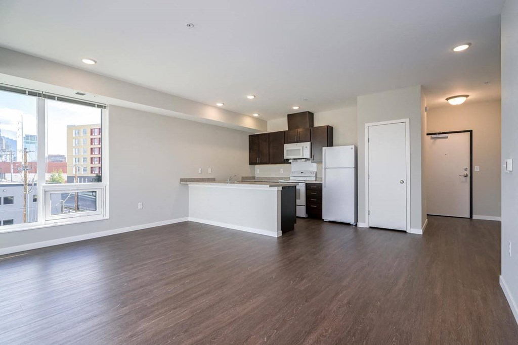 an empty living room with a kitchen and a large window