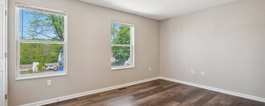a bedroom with two windows and a hardwood floor