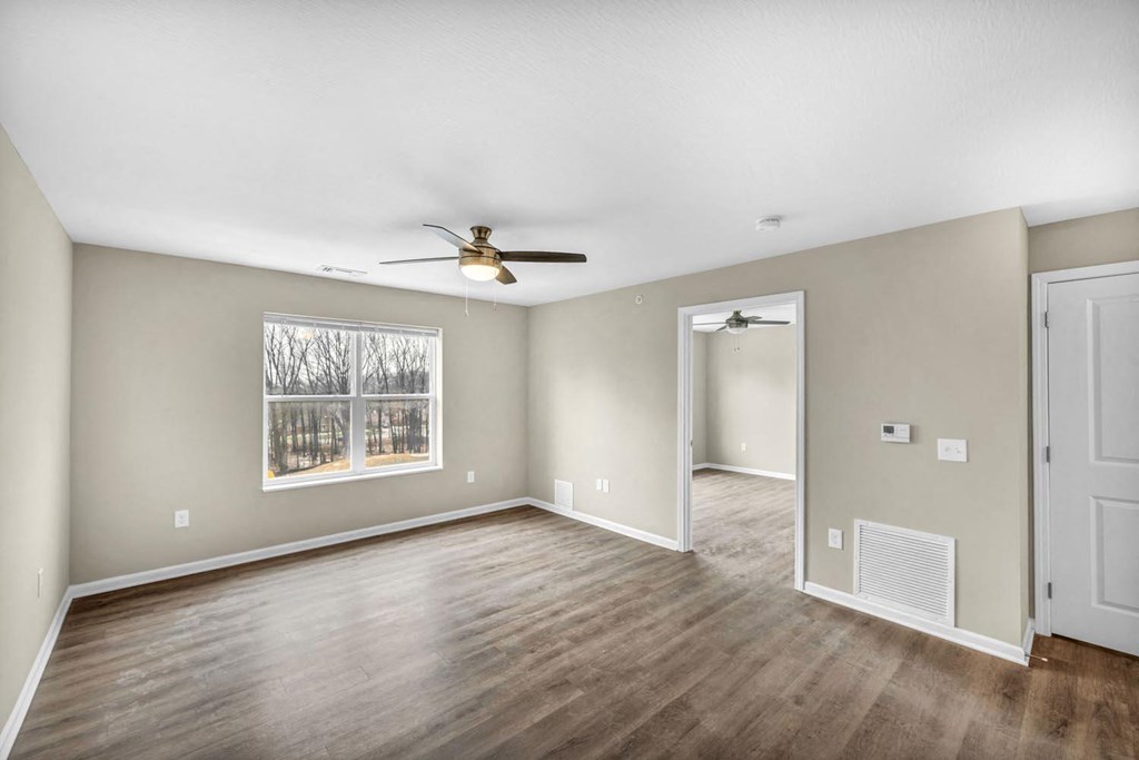 an empty living room with a ceiling fan and a window