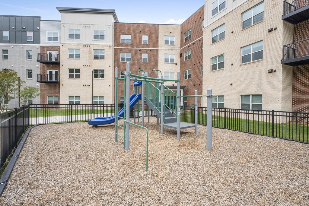 A playground with a slide and a swing set in front of apartment buildings.