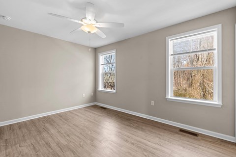 A room with a ceiling fan and a window with a view of trees.