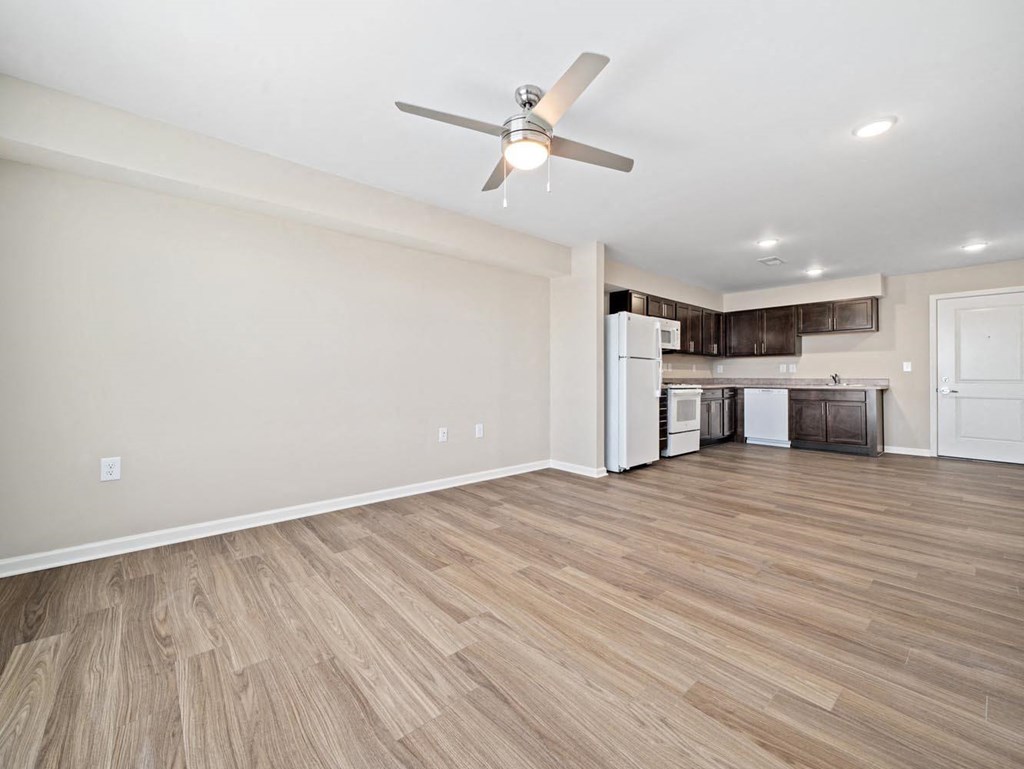 an empty living room with a ceiling fan and a kitchen