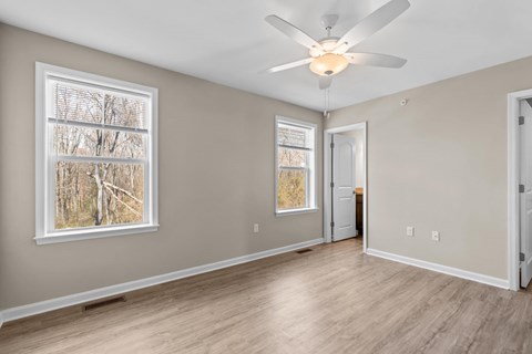 A room with a ceiling fan and a window with a view of trees.