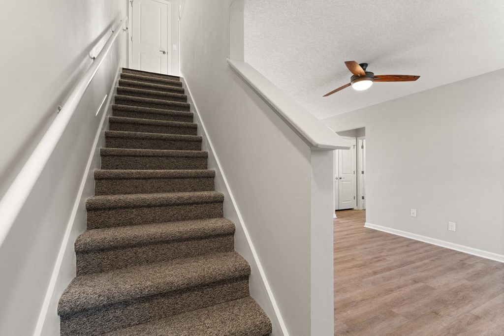 A staircase with a carpeted runner and a ceiling fan.
