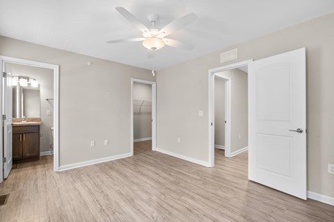 A spacious room with a ceiling fan and light, hardwood floors, and white doors.