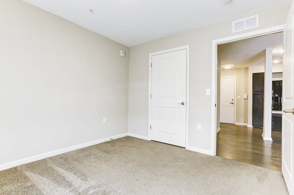 an empty room with a white door and a hallway to a bedroom and a bathroom