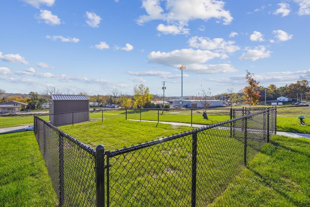 A black fence encloses a grassy area with a blue sky and clouds in the background.