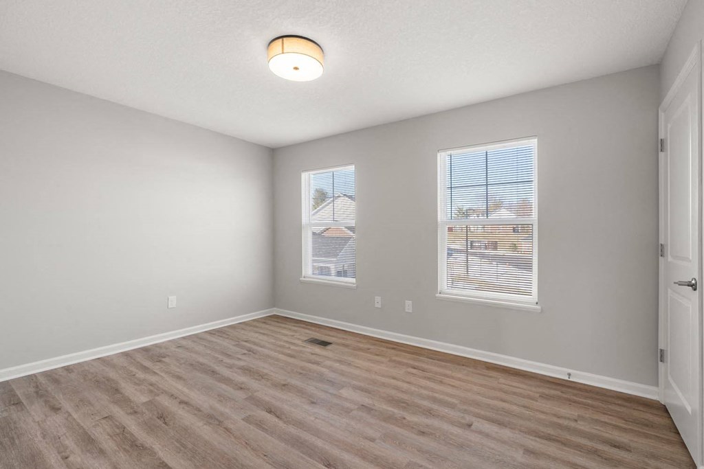 A room with light wood flooring and two windows.