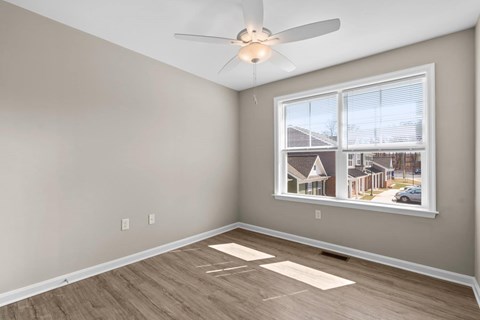 A room with a ceiling fan and a window showing a residential area outside.