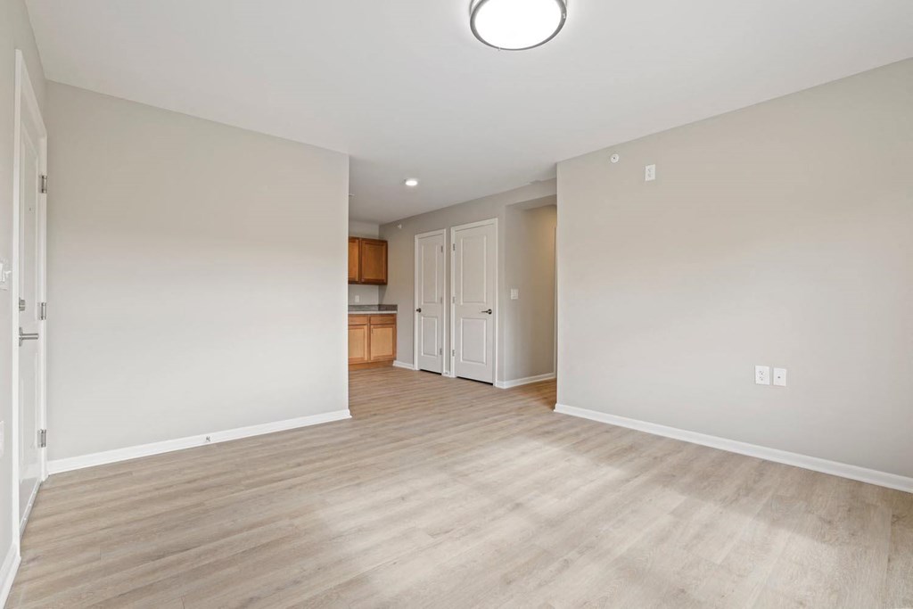 an empty living room and kitchen with wood flooring and white walls
