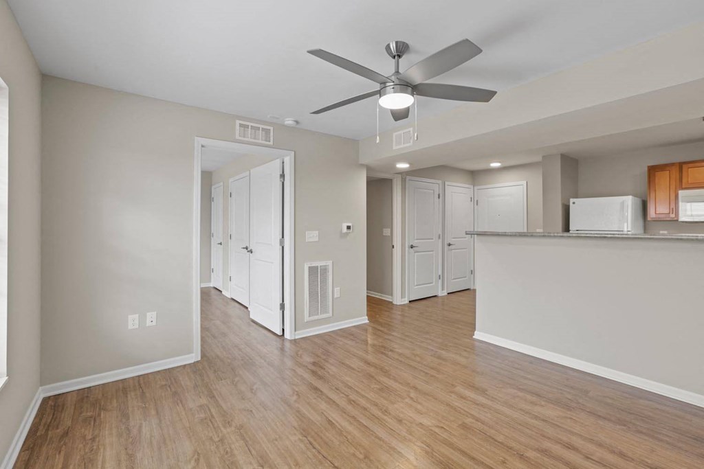 an empty living room with a ceiling fan and a kitchen