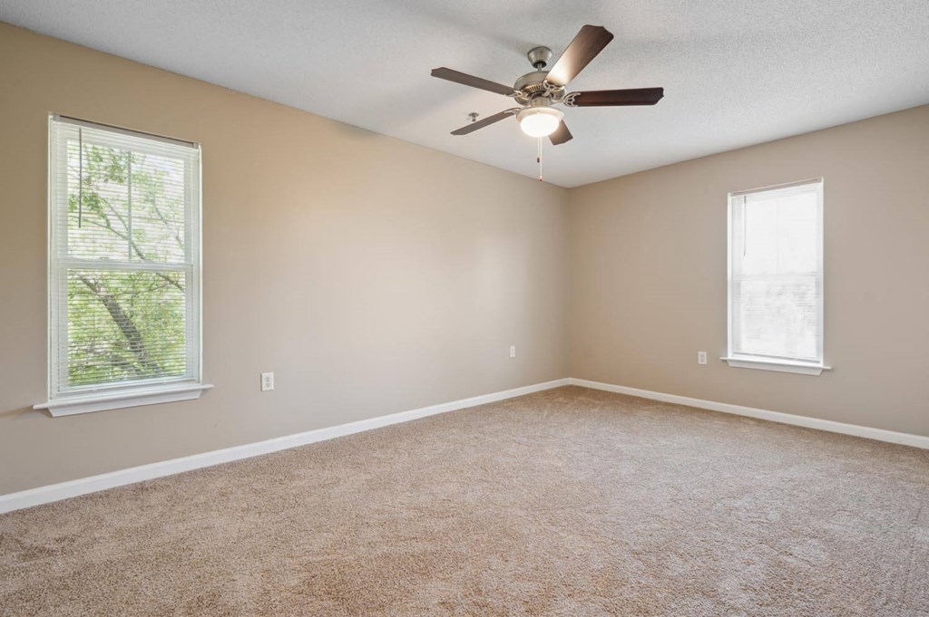 an empty room with a ceiling fan and two windows