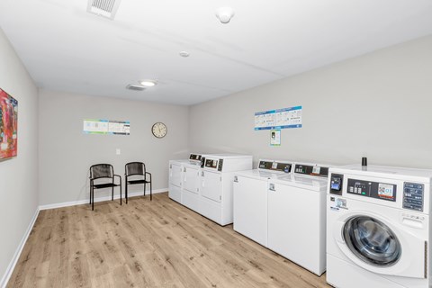 A laundry room with a washer and dryer on the right and two chairs on the left.