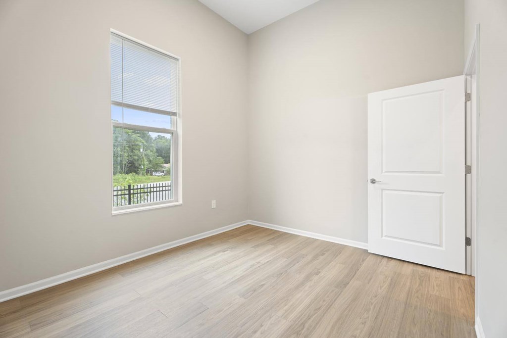 A room with a white door and a window with a view of a fence and trees.
