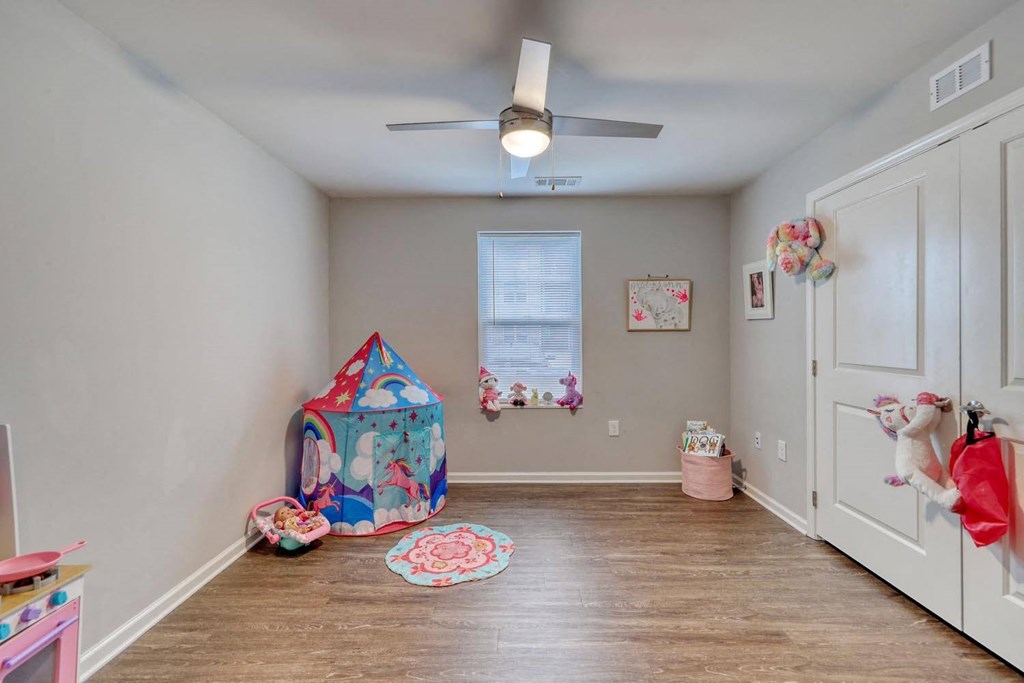 a bedroom with a ceiling fan and a door to a room with a play area