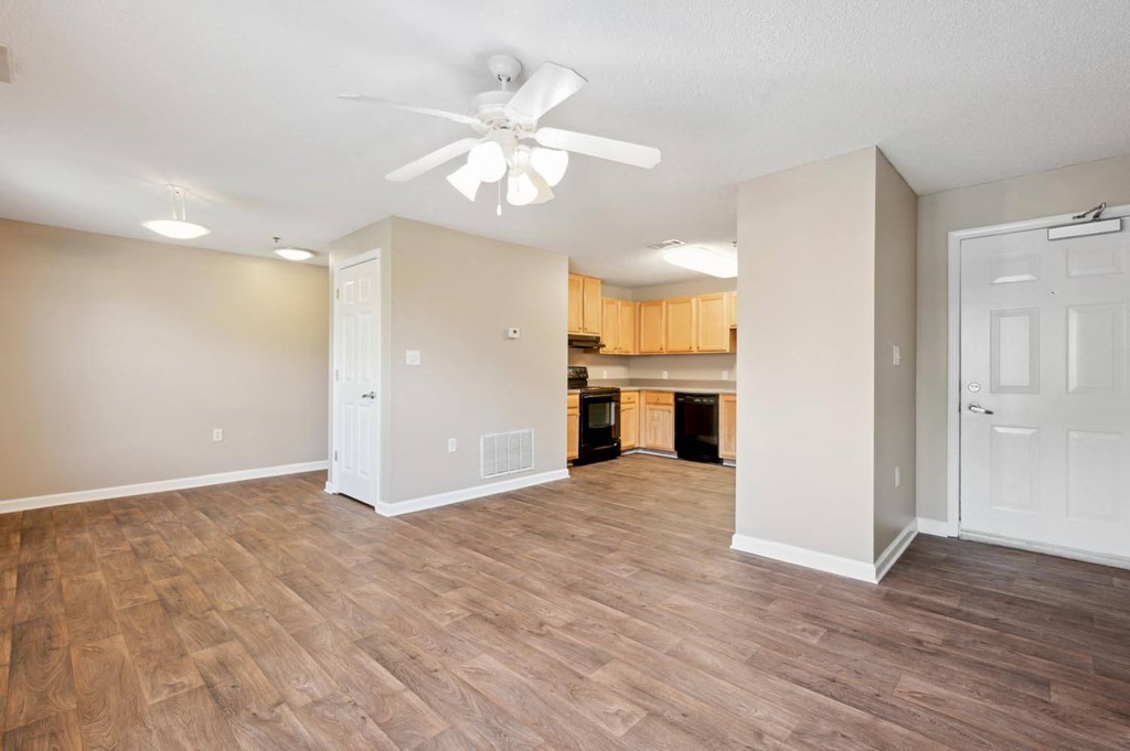 an empty living room with a ceiling fan and a kitchen