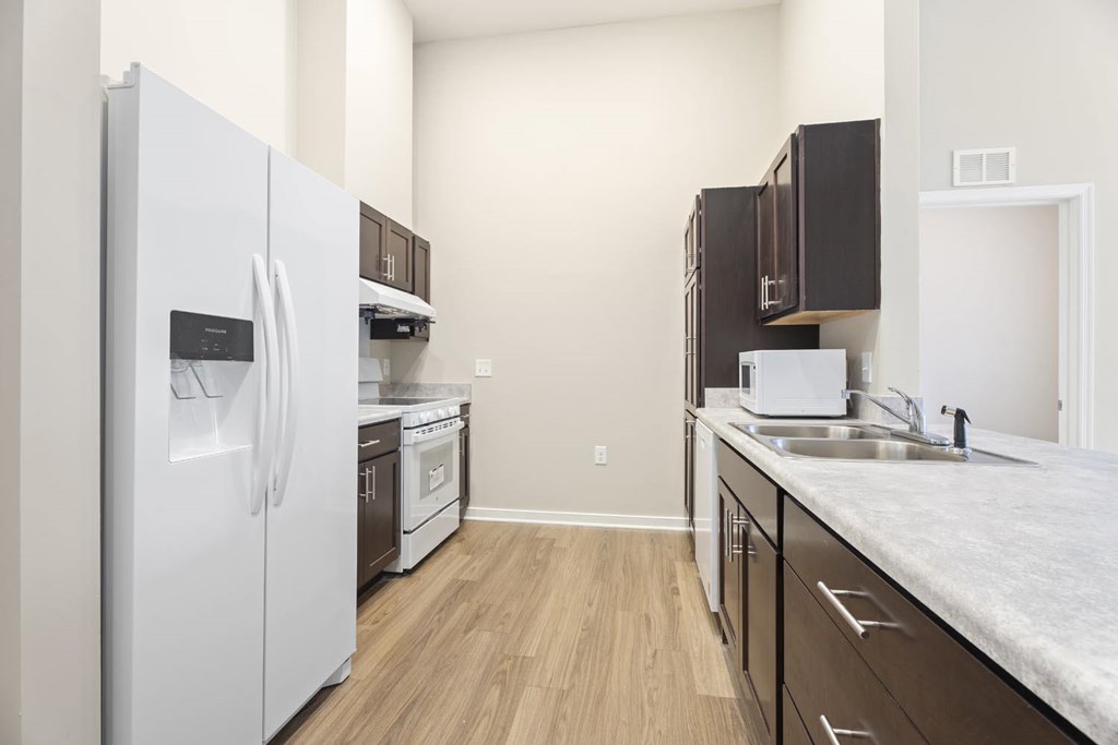 A kitchen with a white refrigerator, wooden cabinets, and a marble countertop.