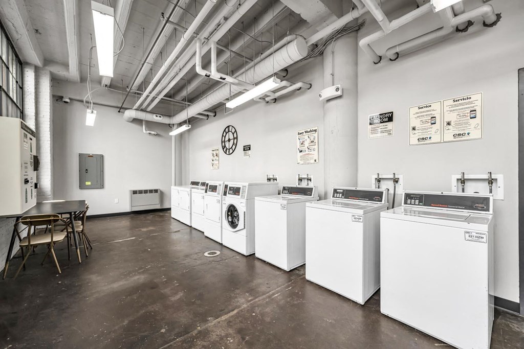 a row of washing machines in a room with a table and chairs