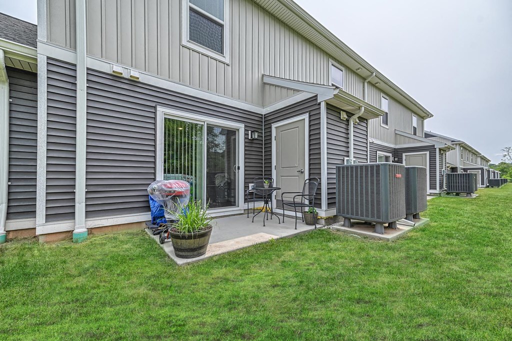 a patio with a grill and chairs on the side of a house