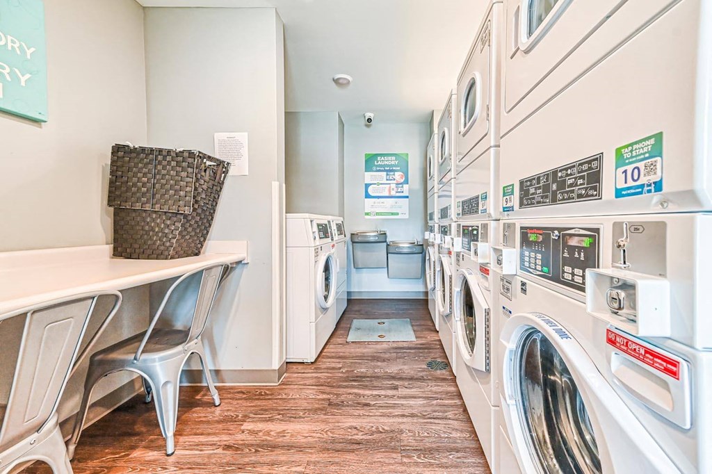 a laundry room with white washers and dryers and a table with a chair