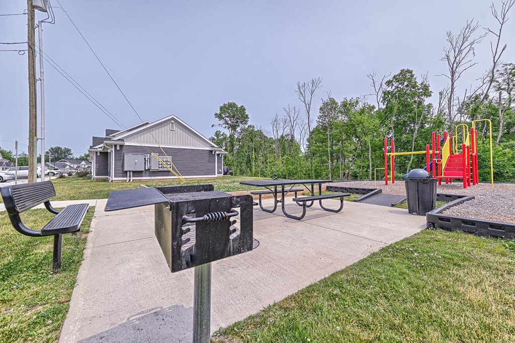 a picnic area with a picnic table and benches and a playground in the background