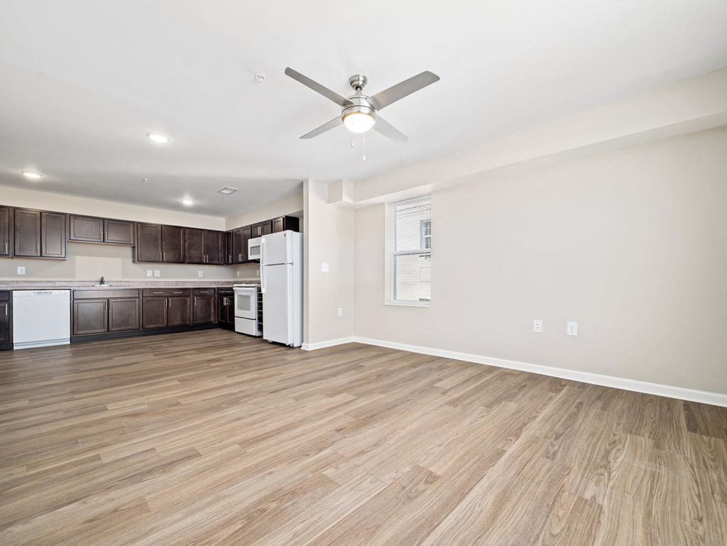 an empty living room with a ceiling fan and a kitchen