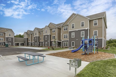 A playground with a slide and picnic table in front of apartment buildings.