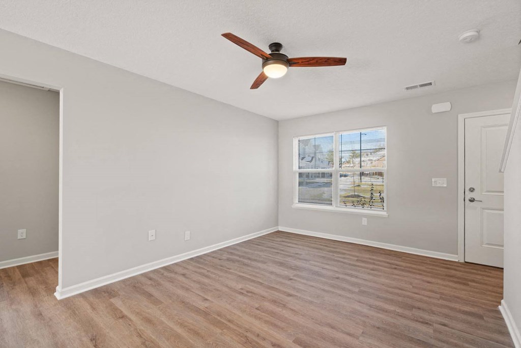 A room with a ceiling fan and a window showing a view of a street.